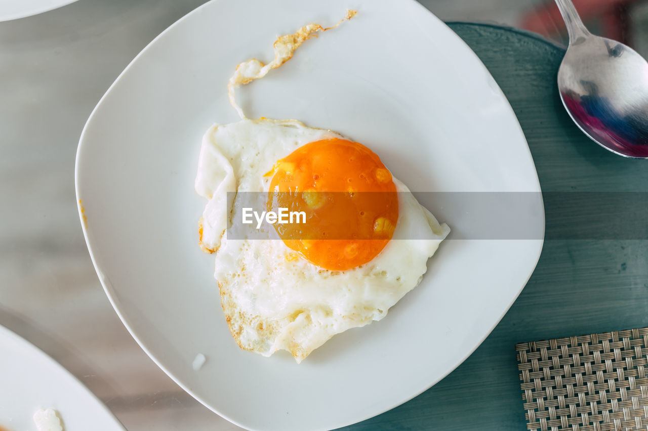 Top view of white plate with fried egg on glass table background