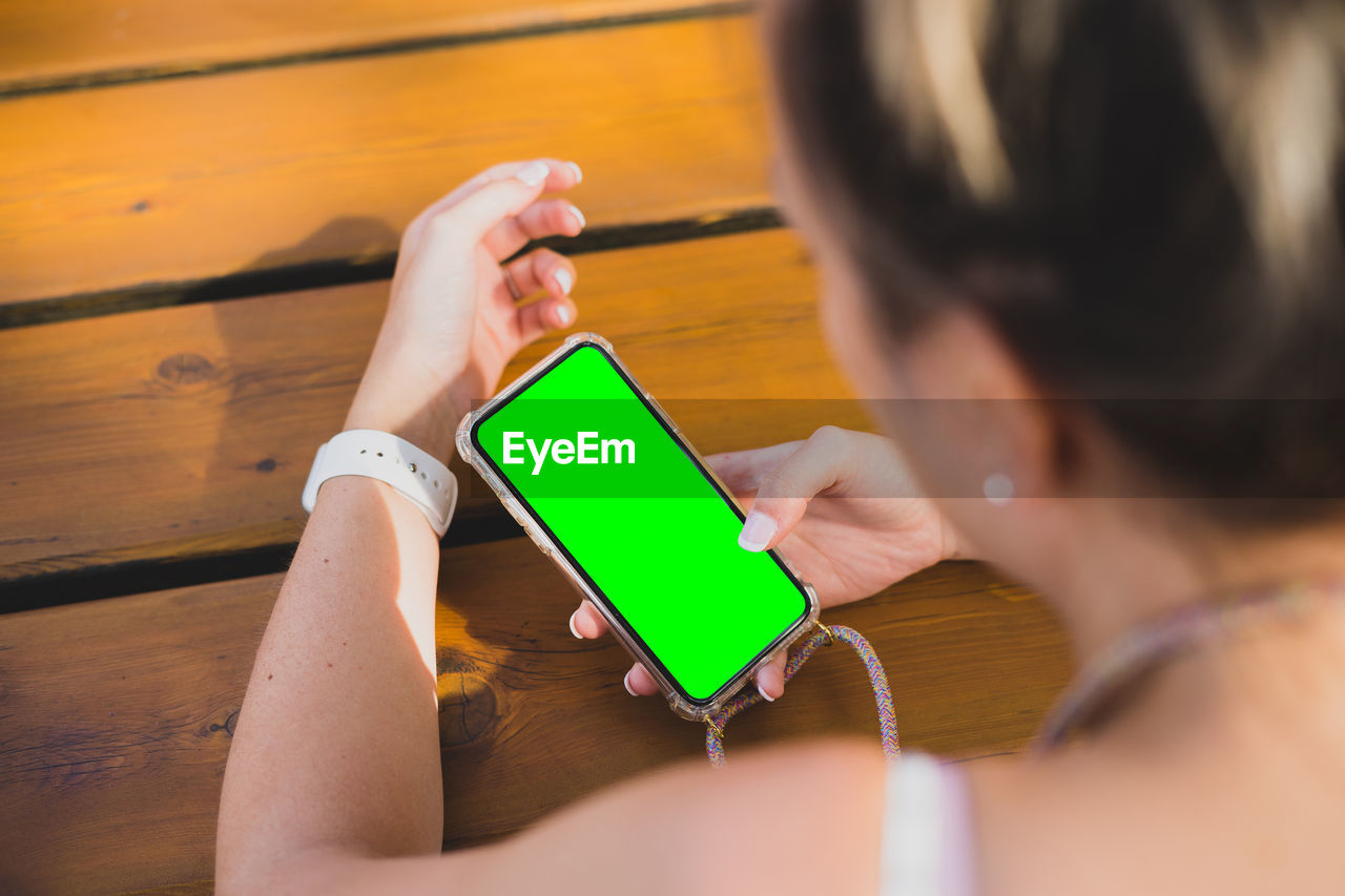 PORTRAIT OF WOMAN USING MOBILE PHONE WHILE SITTING ON TABLE