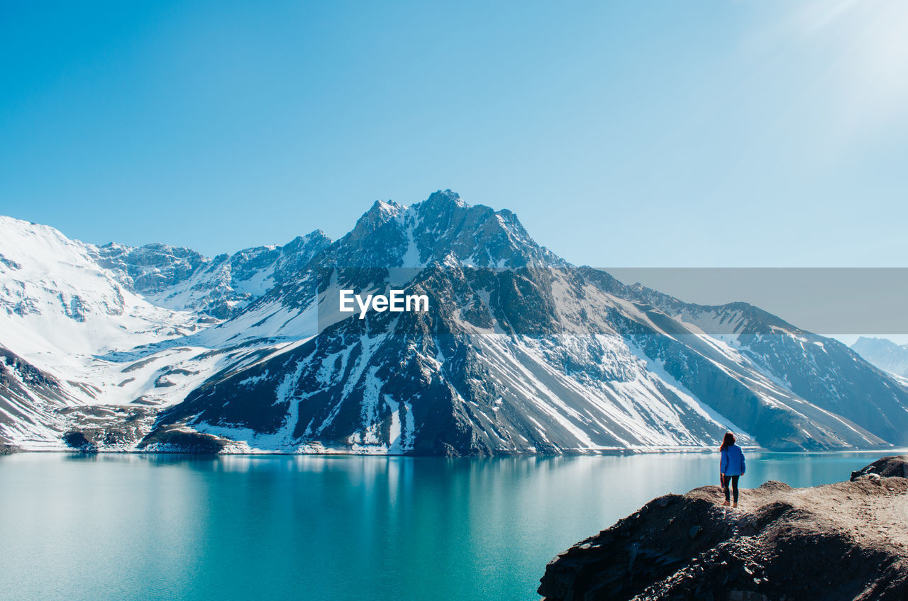 Rear view of woman standing by lake against mountain