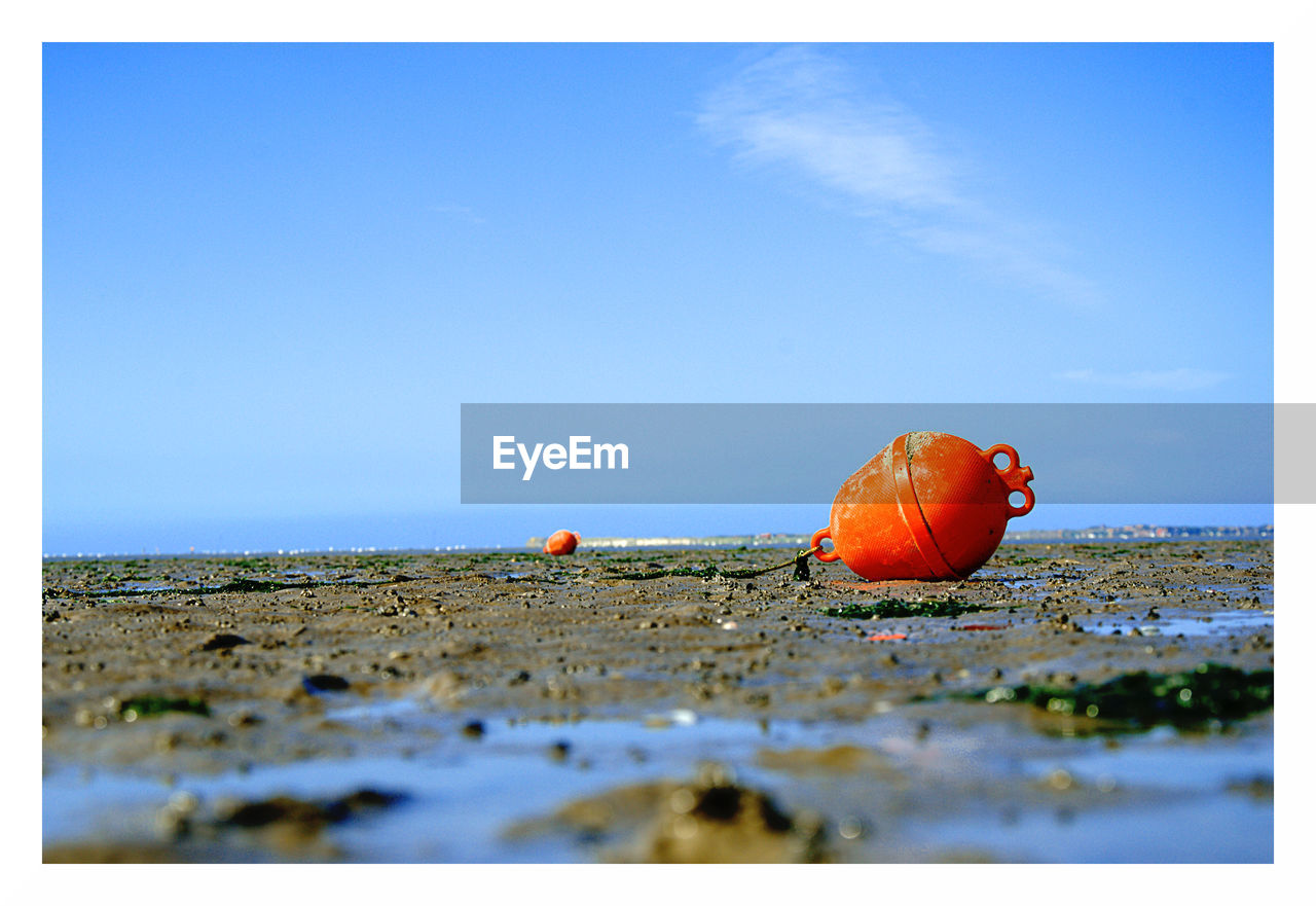 Orange buoy on beach against sky