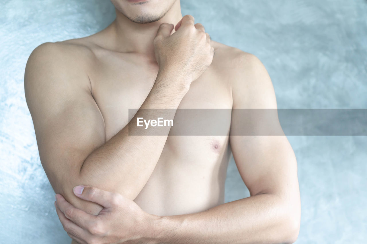MIDSECTION OF SHIRTLESS MAN LYING ON BED