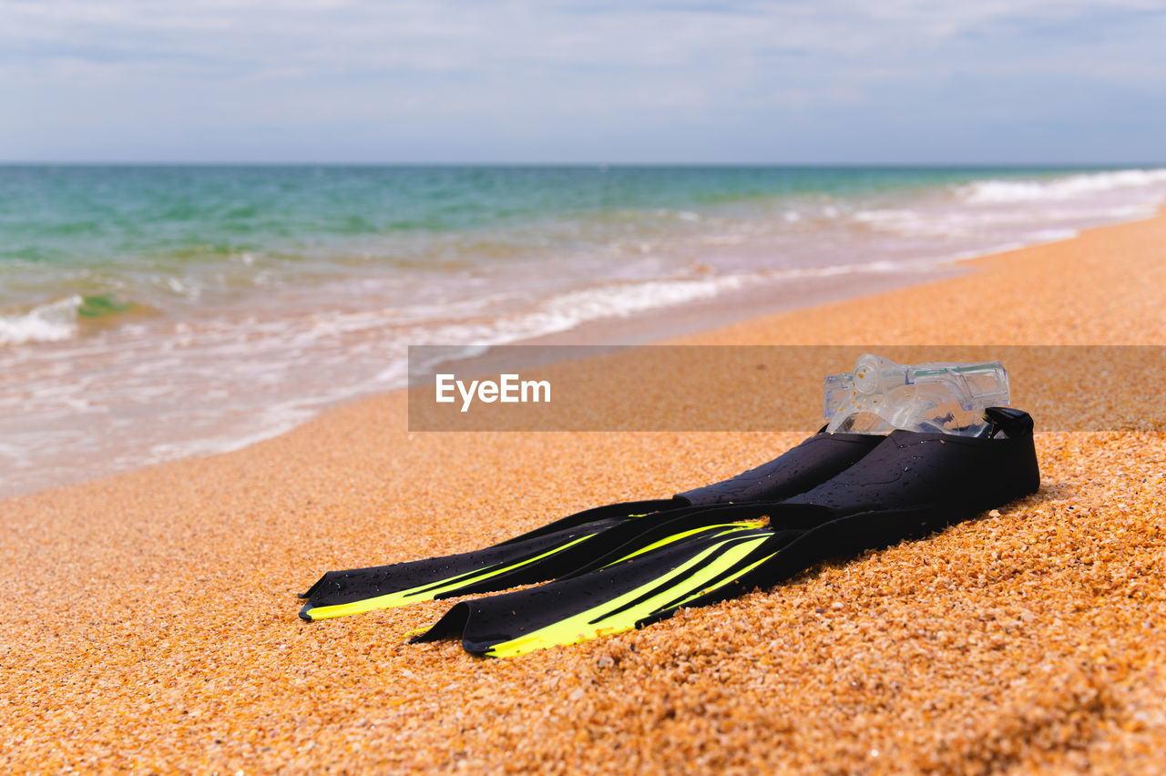 Snorkeling mask with fins lies on a sandy beach overlooking the sea and sky, no people