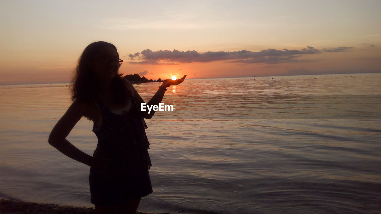 Optical illusion of woman holding sun at beach during sunset