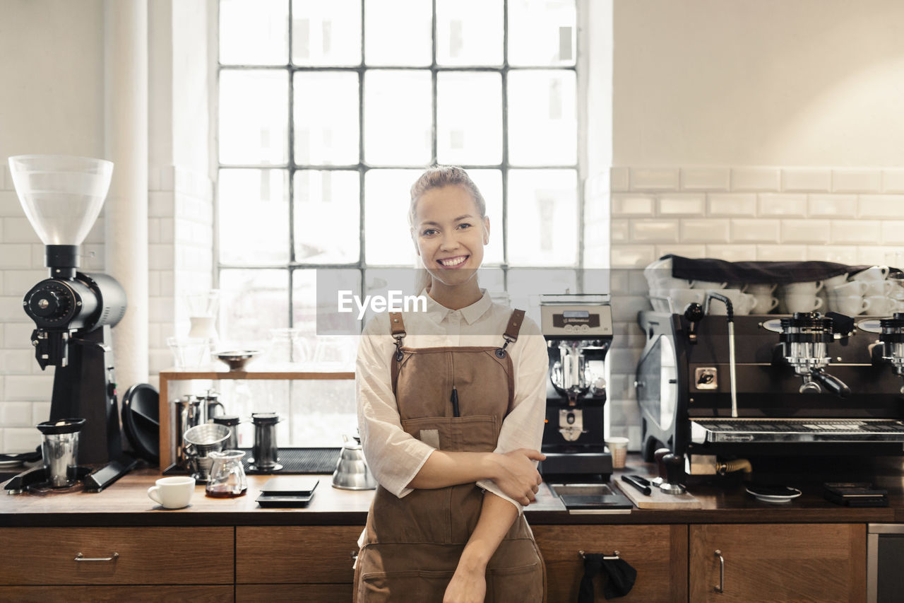 Portrait of happy female barista standing by counter in coffee shop