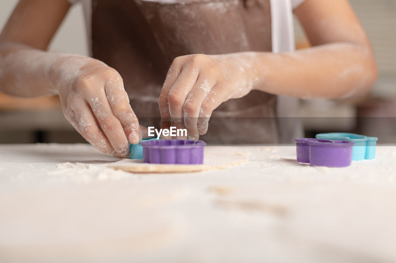 A little asian girl is using a blue mold to cut the dough for making cookies in the kitchen.