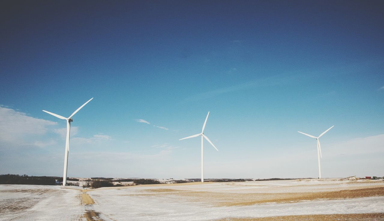 Windmills on field against blue sky during sunny day