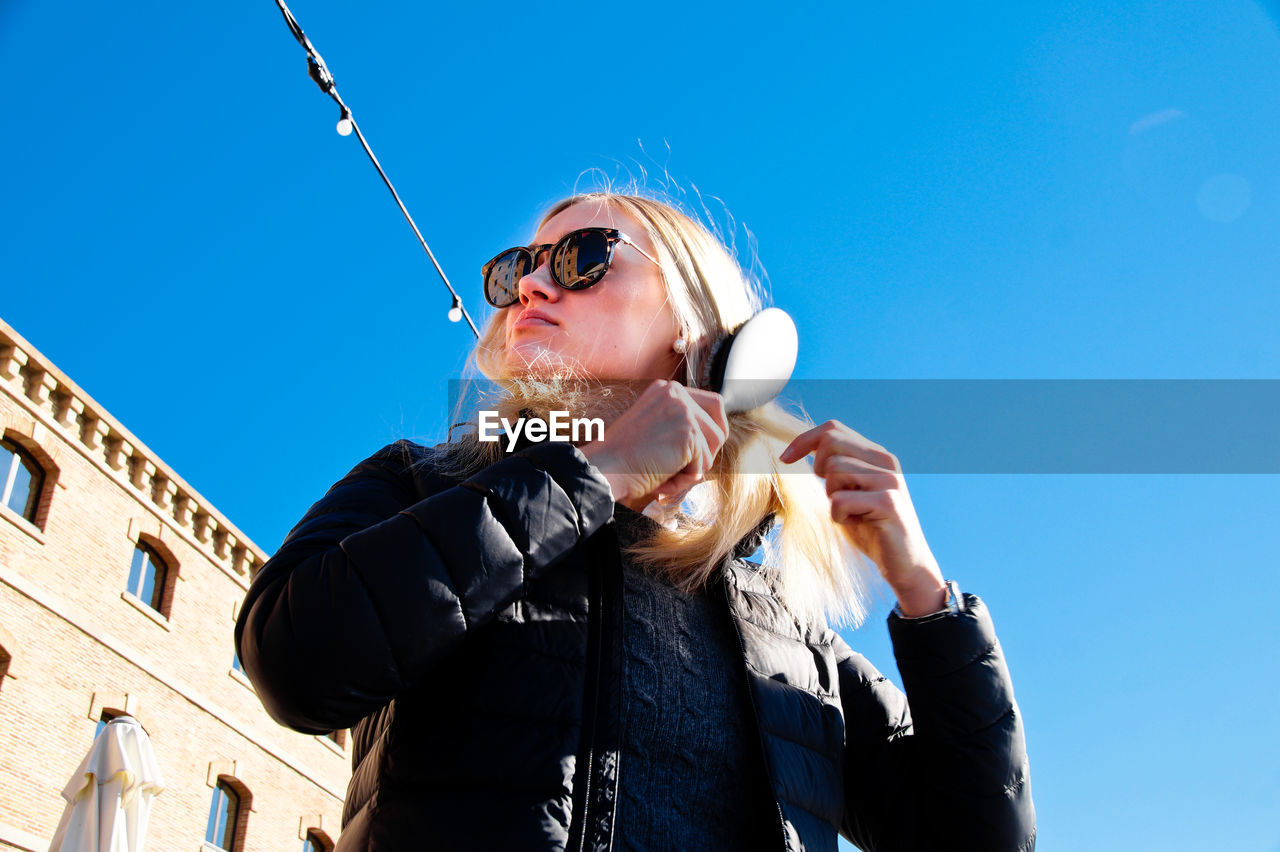 Low angle view of woman combing hair against clear sky