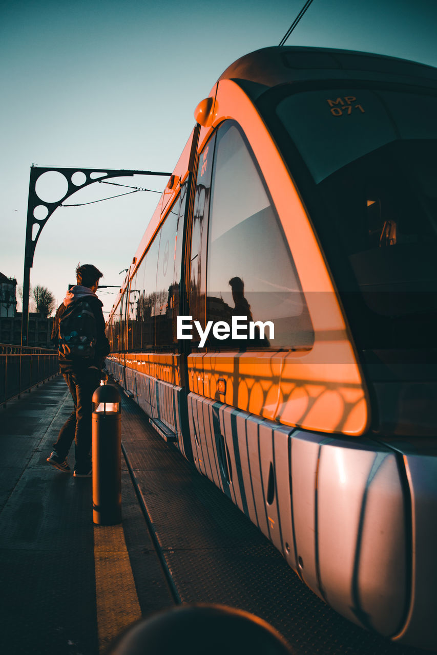 Rear view of man at railroad station against sky during sunset