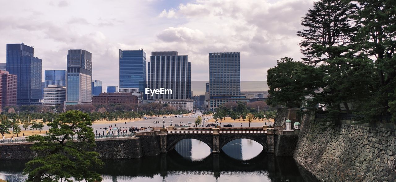 Bridge over river amidst buildings in city against sky