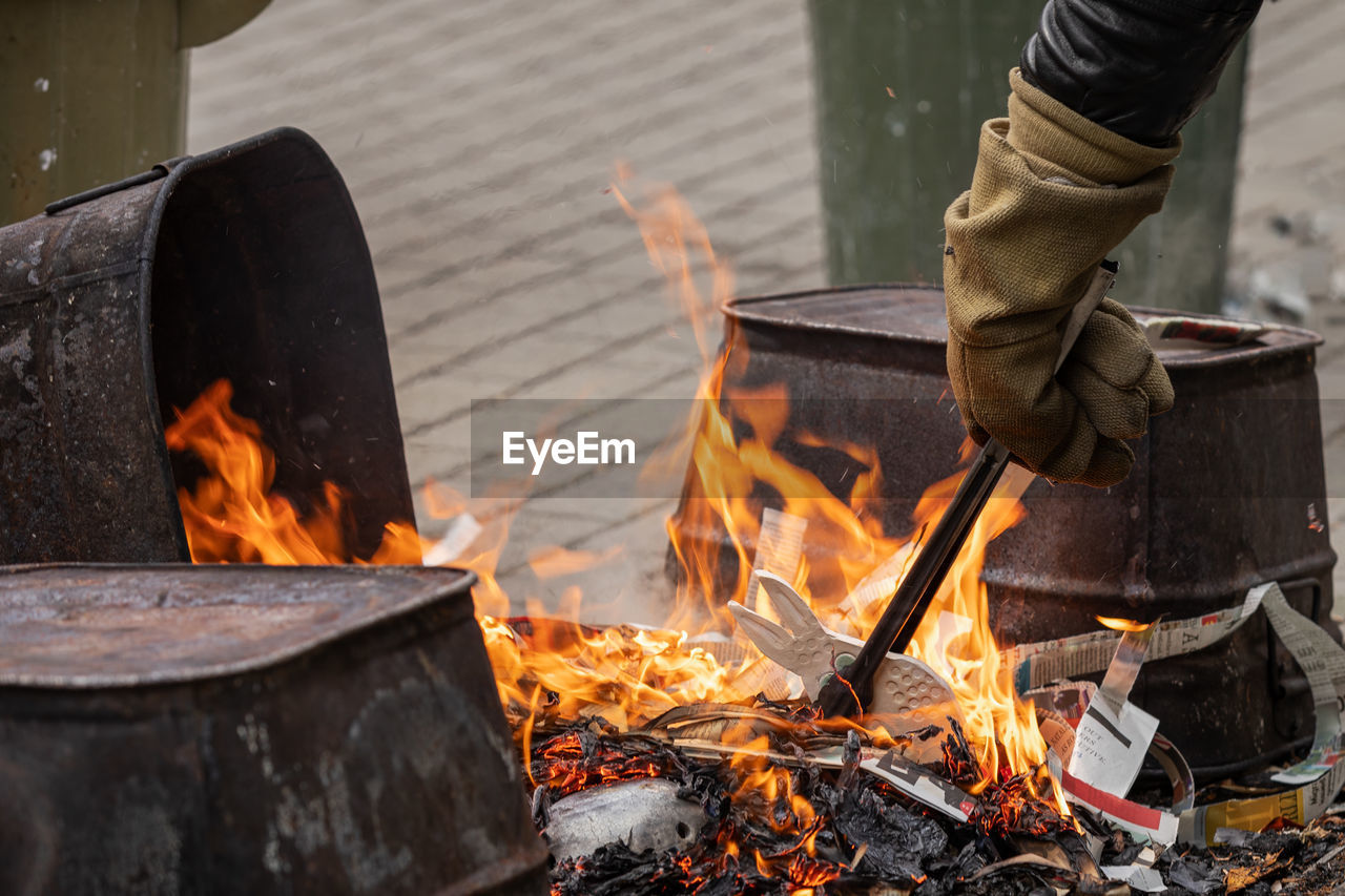 A cropped hand wearing fire resistant gloves places raku ware into a reduction fire tongs