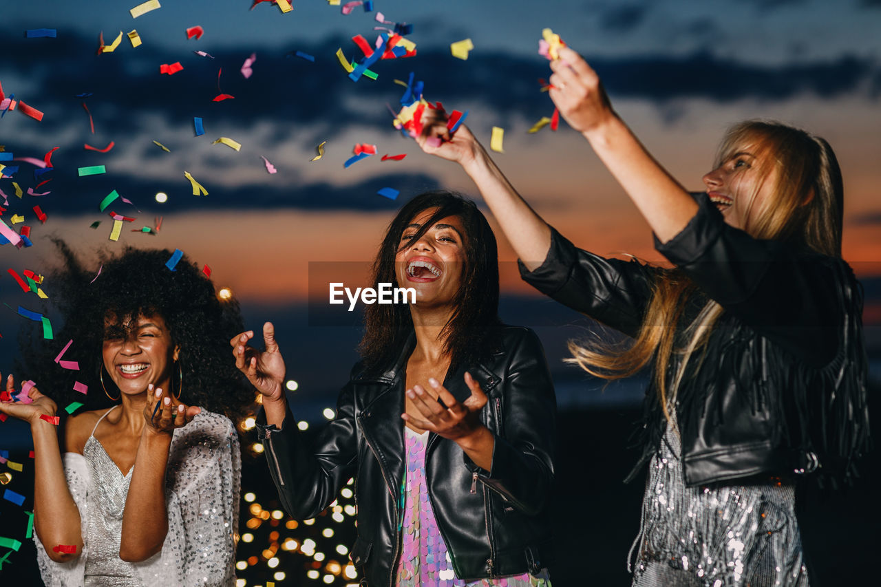 Cheerful friends with confetti enjoying at beach during sunset