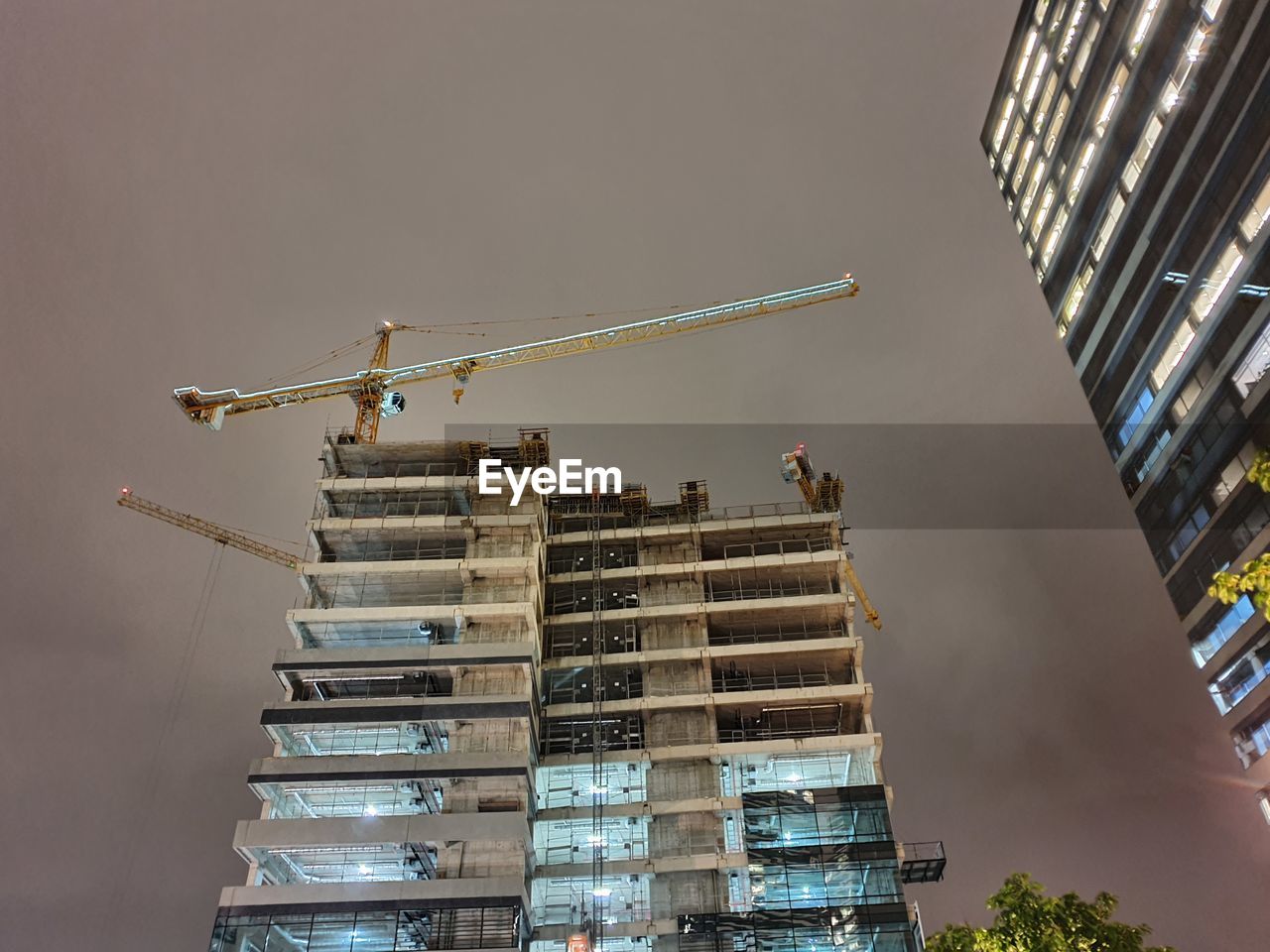 Low angle view of crane by building against sky