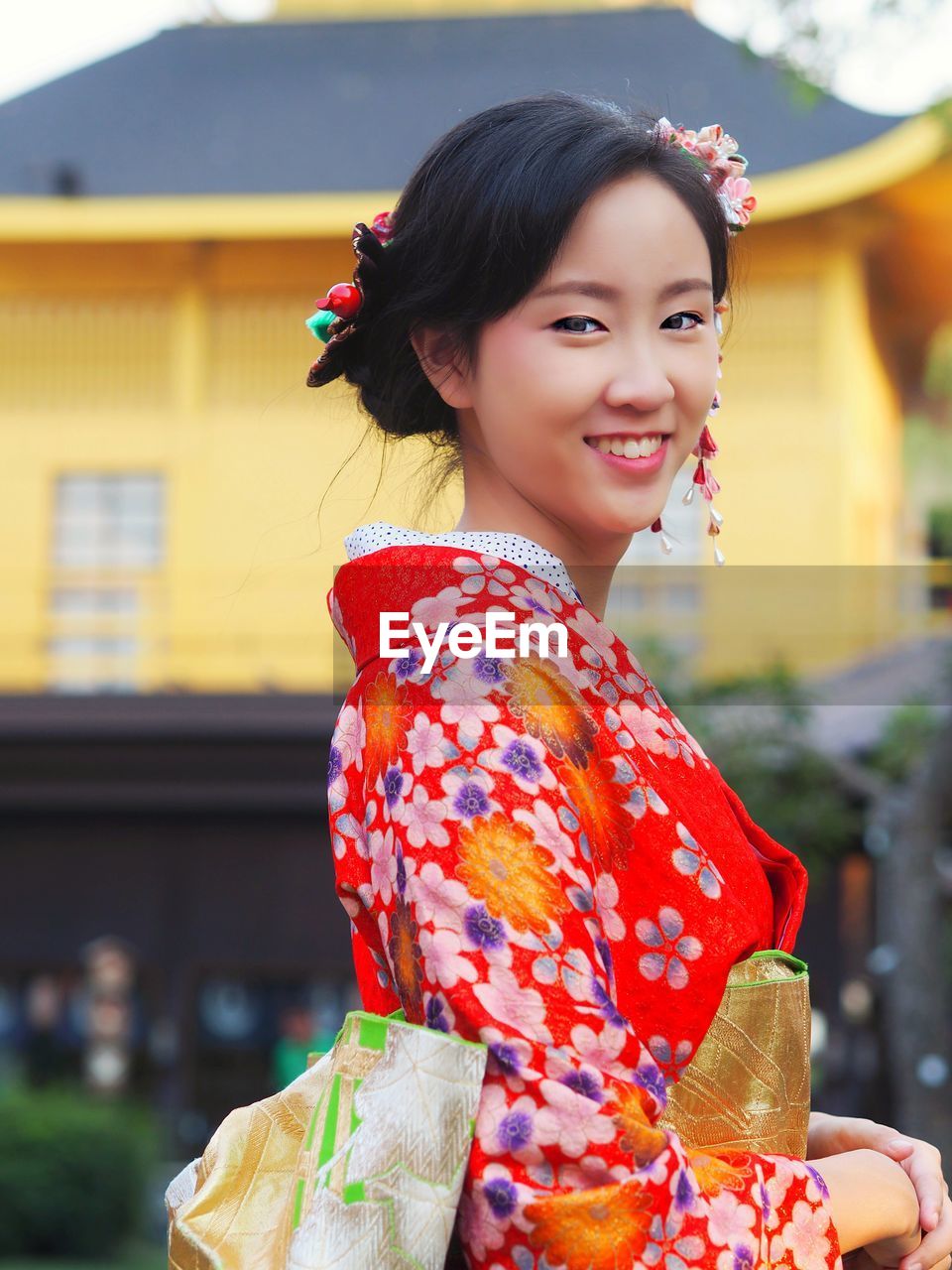 Portrait of smiling young woman in traditional clothing standing against house