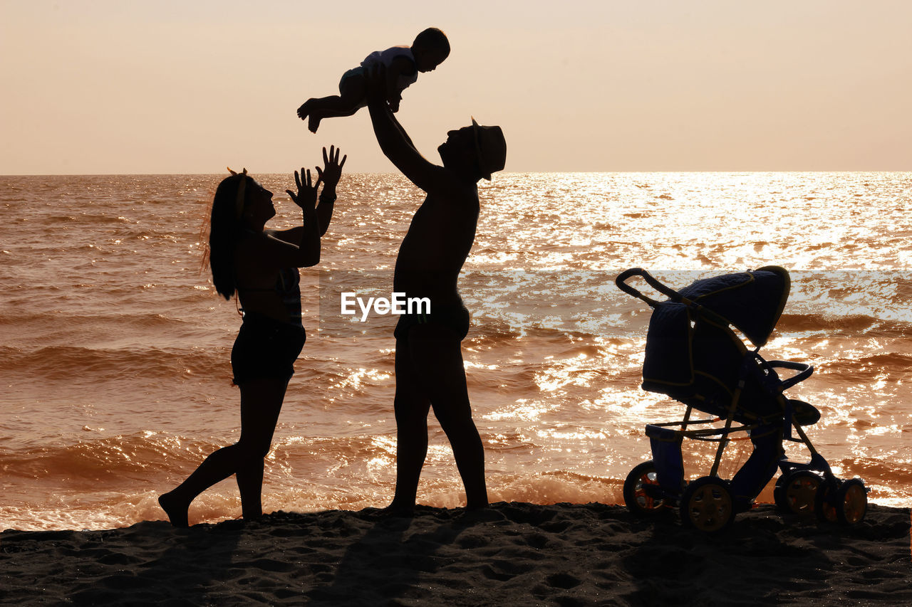 Silhouette family at beach against sky during sunset