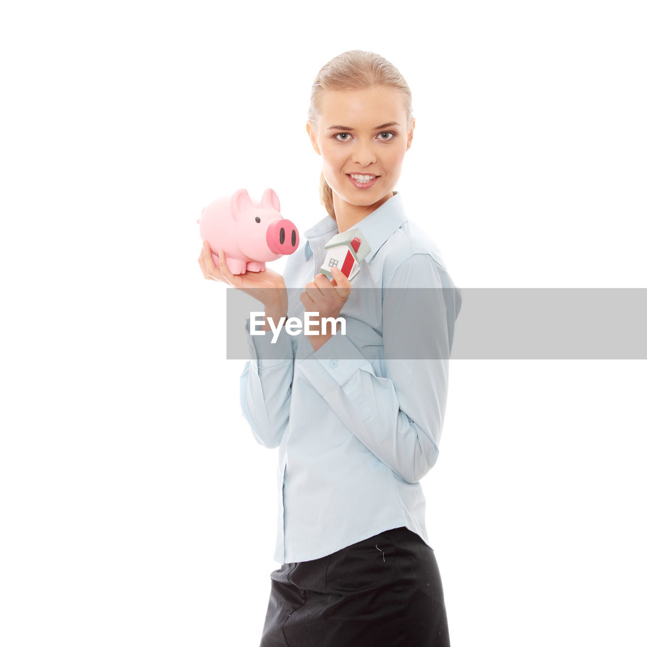 Portrait of real estate agent with piggy bank and model home standing against white background
