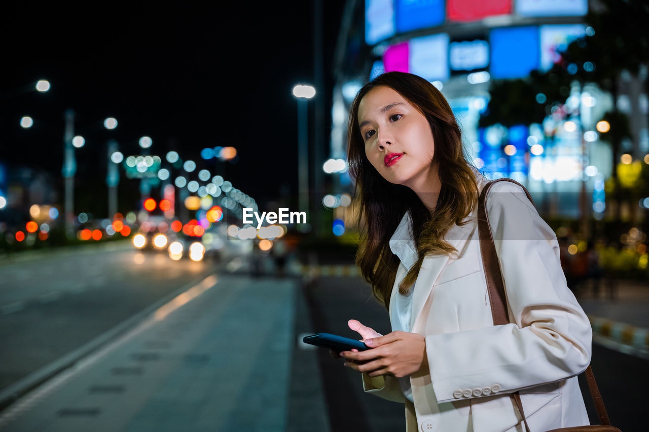 portrait of young woman standing against illuminated city