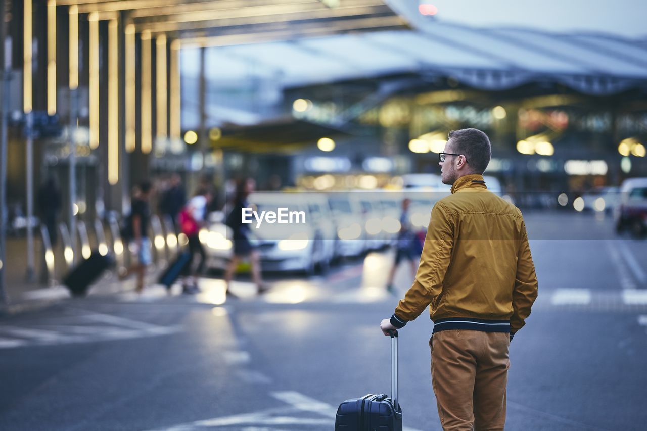 Rear view of mid adult man with luggage standing on street at airport