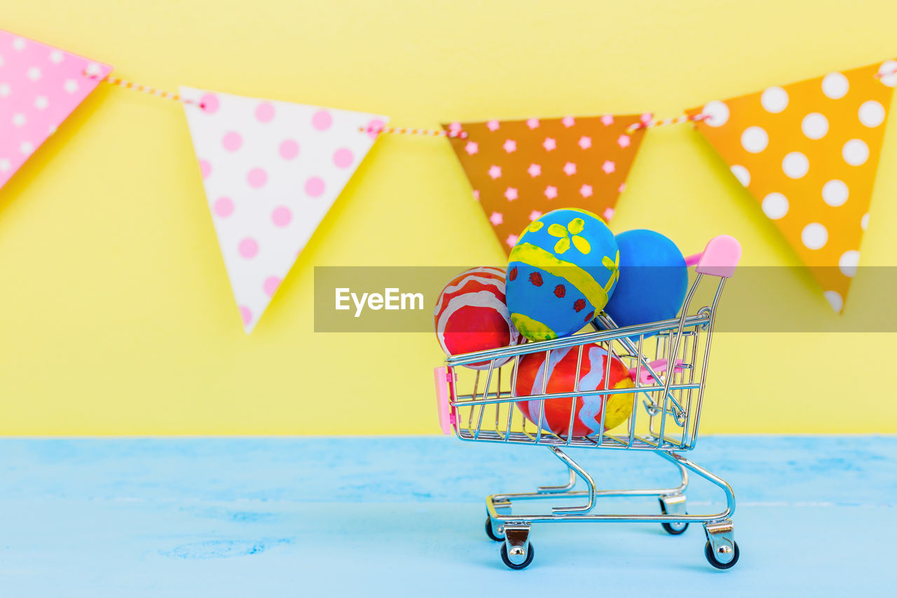 Easter eggs in toy shopping cart on table against bunting