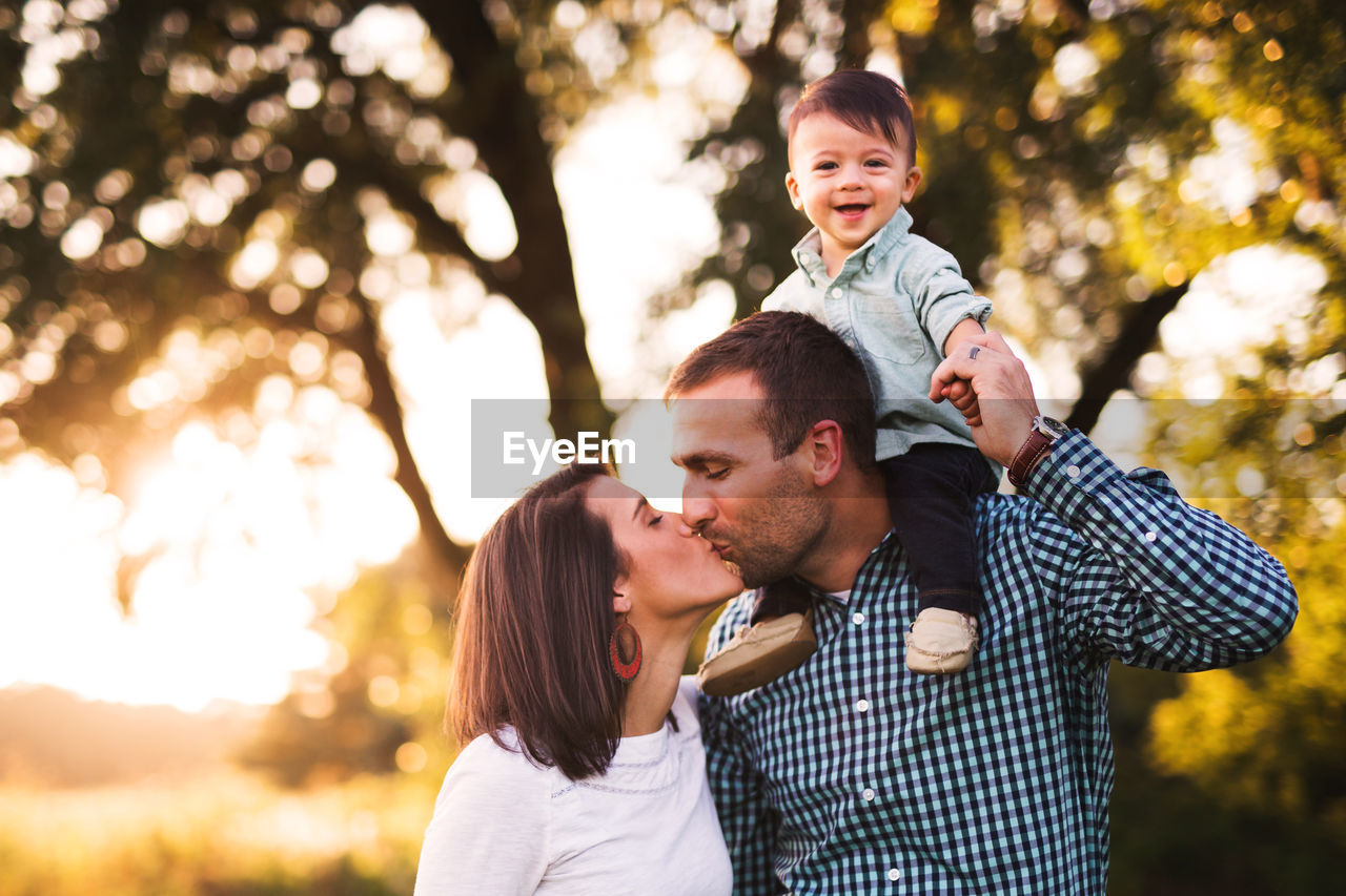 Portrait of cute smiling baby boy while parents kissing in park