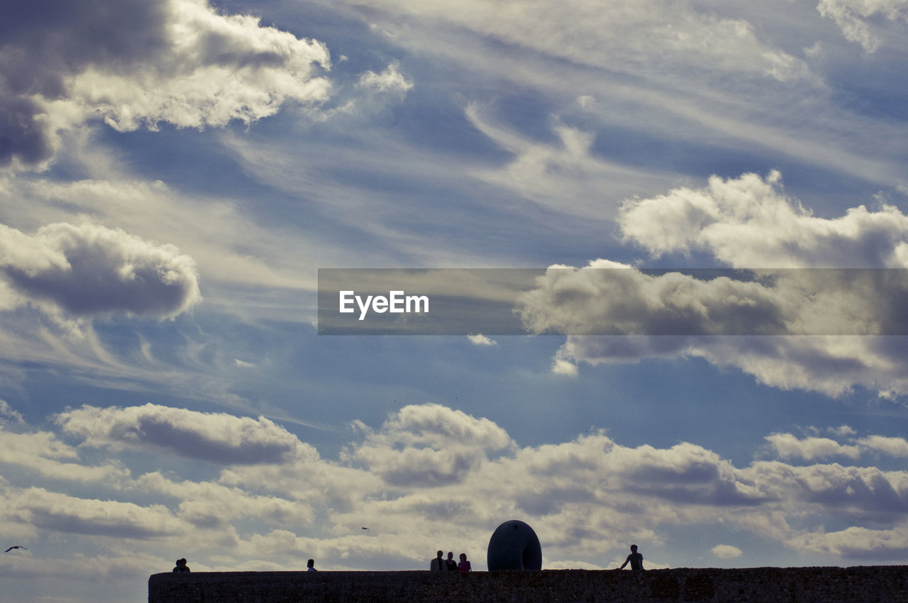 Low angle view of people on building terrace against cloudy sky