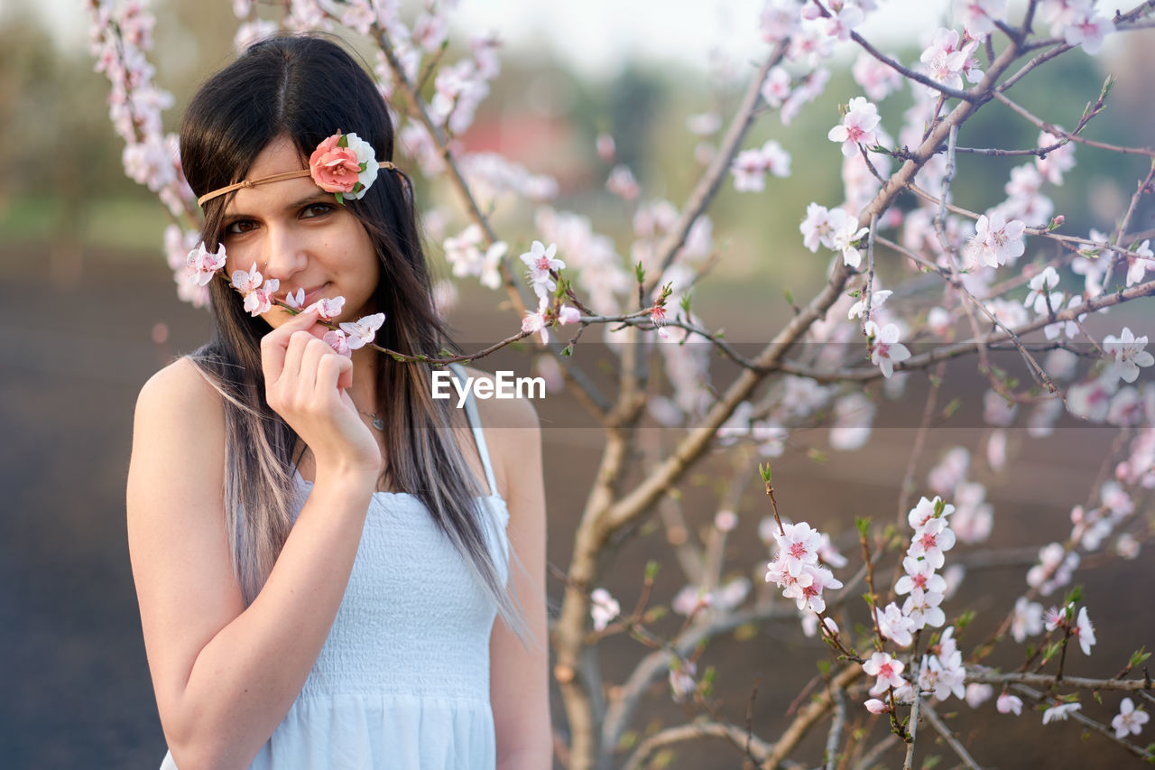 Portrait of young woman standing by cherry tree