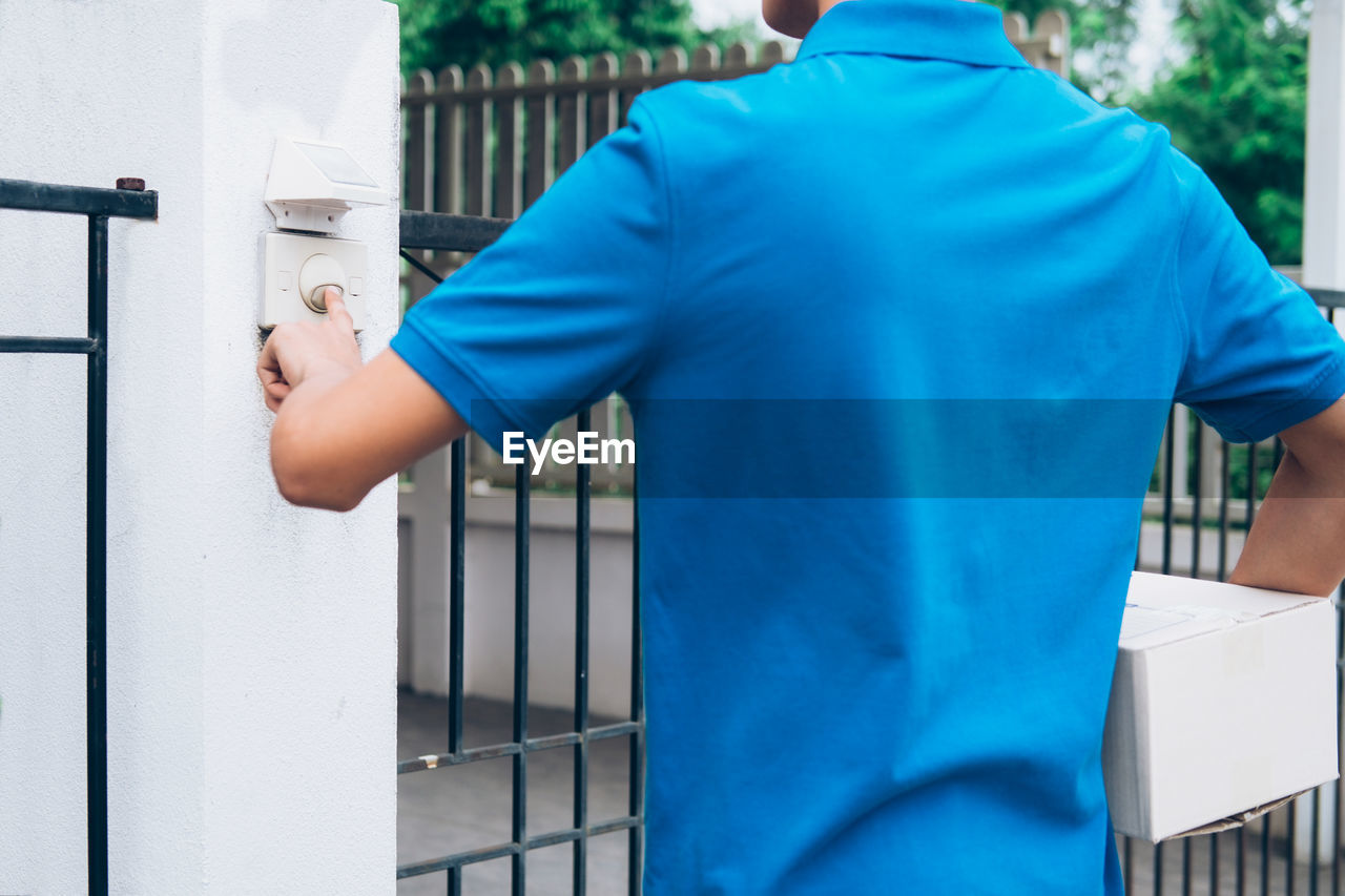 Delivery man pressing door bell while standing at gate