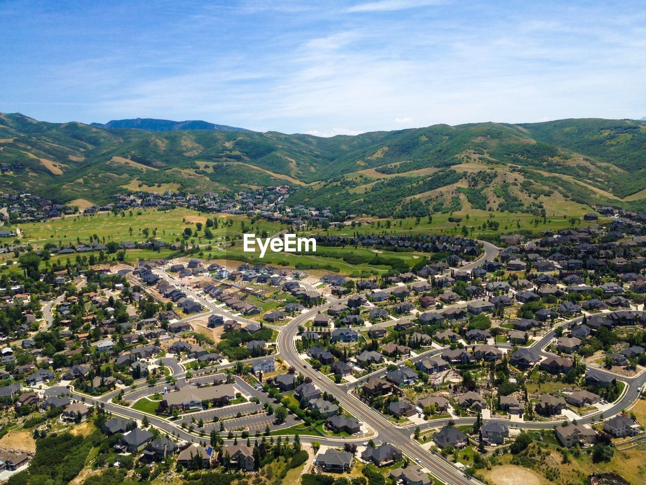 Aerial view of houses in city by mountains against cloudy sky