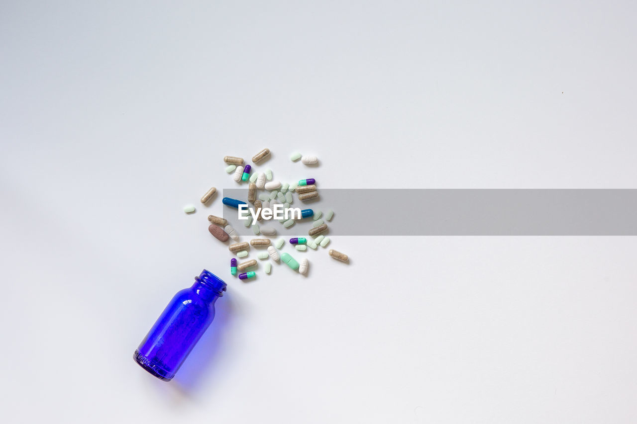studio shot, white background, indoors, hand, jewellery, copy space, fashion accessory, high angle view, finger, still life, large group of objects, multi colored, blue, capsule, pill