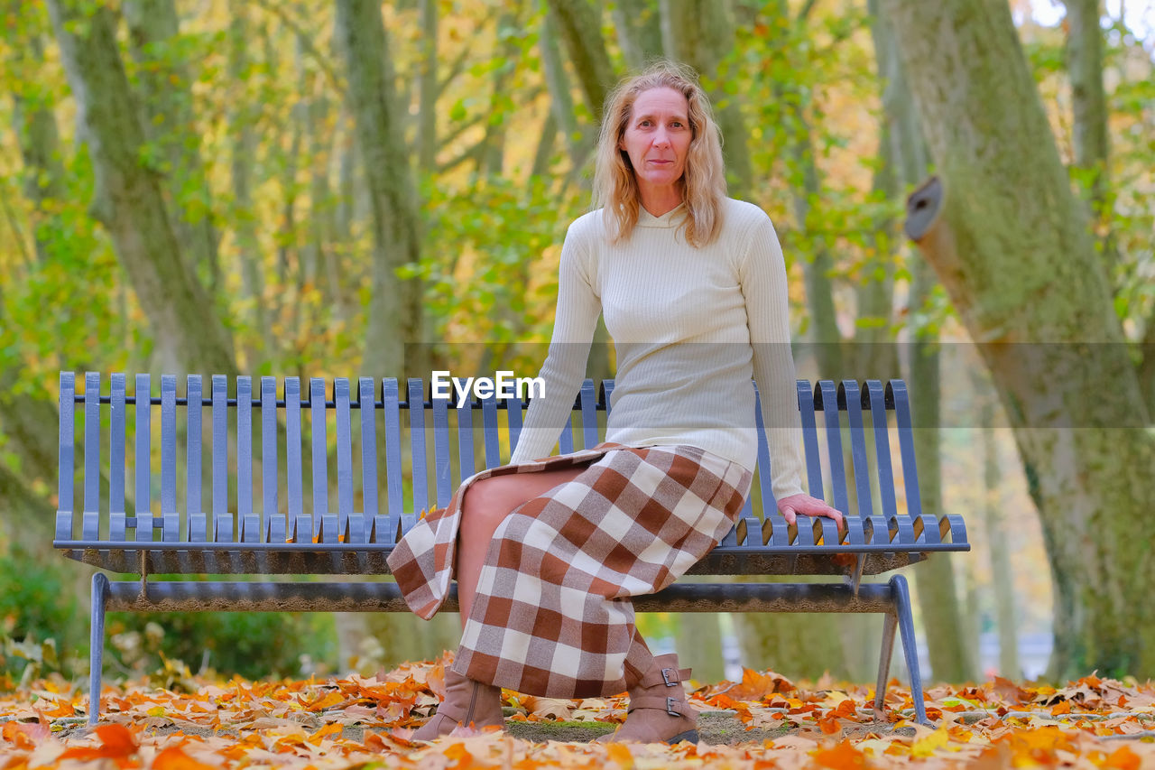 Portrait of smiling woman sitting on seat against trees