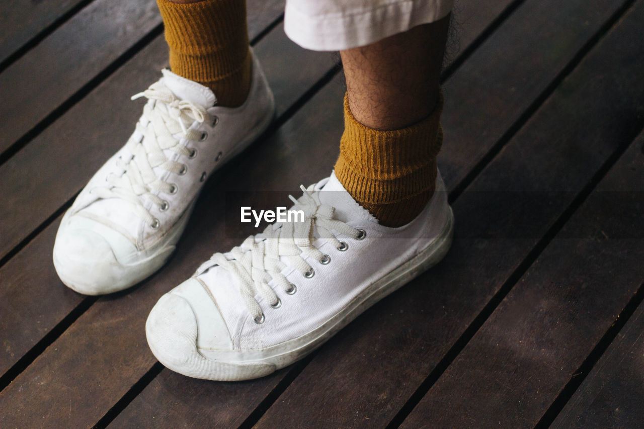 Low section of man wearing white canvas shoes on floor