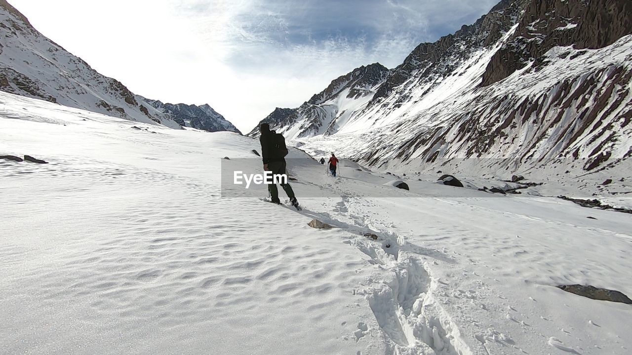 PEOPLE WALKING ON SNOWCAPPED MOUNTAINS AGAINST SKY