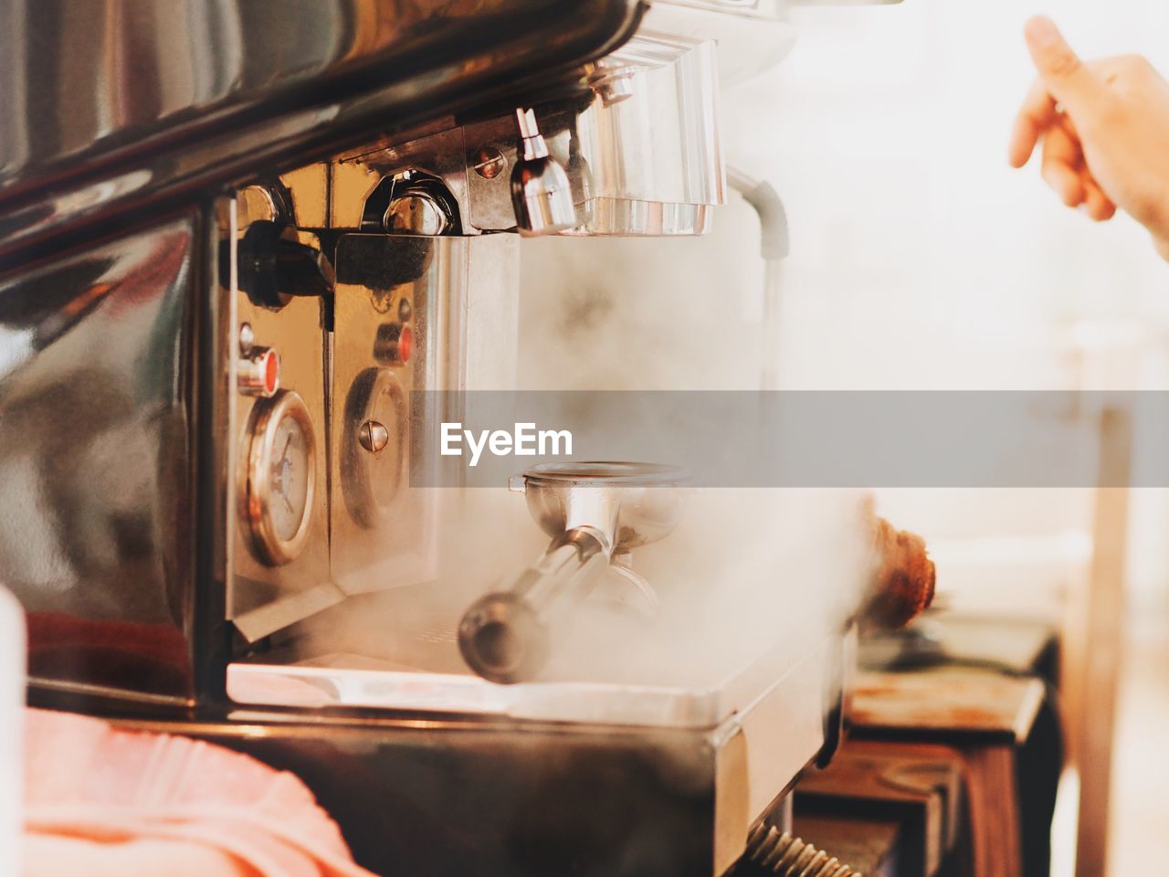 Cropped hand of person by steam emitting from espresso maker at cafe