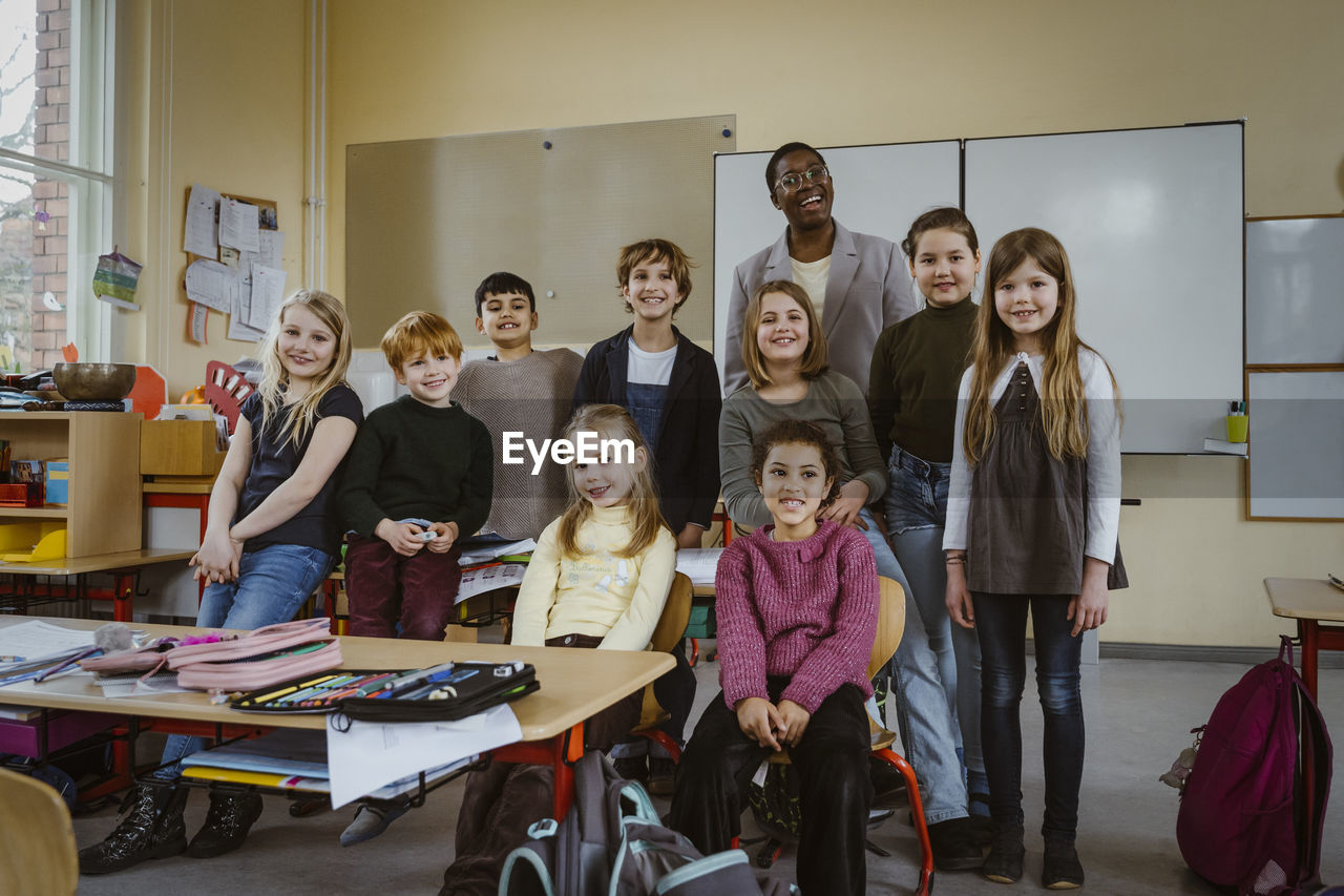 Portrait of smiling teacher and boys and girls against whiteboard in classroom