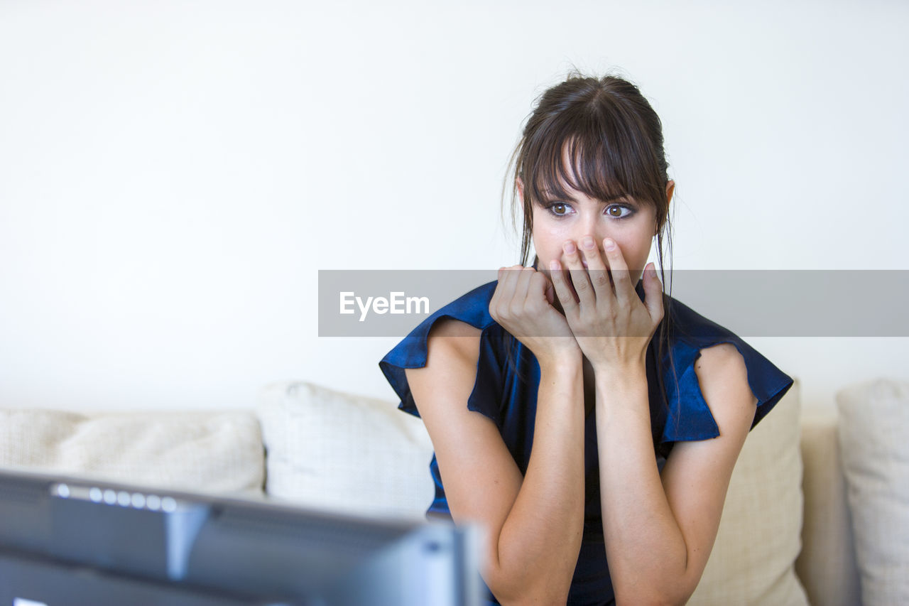 Shocked woman watching television while sitting on sofa at home