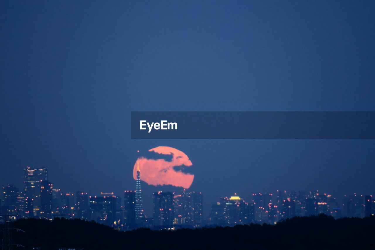 Tokyo tower in illuminated city against sky at dawn