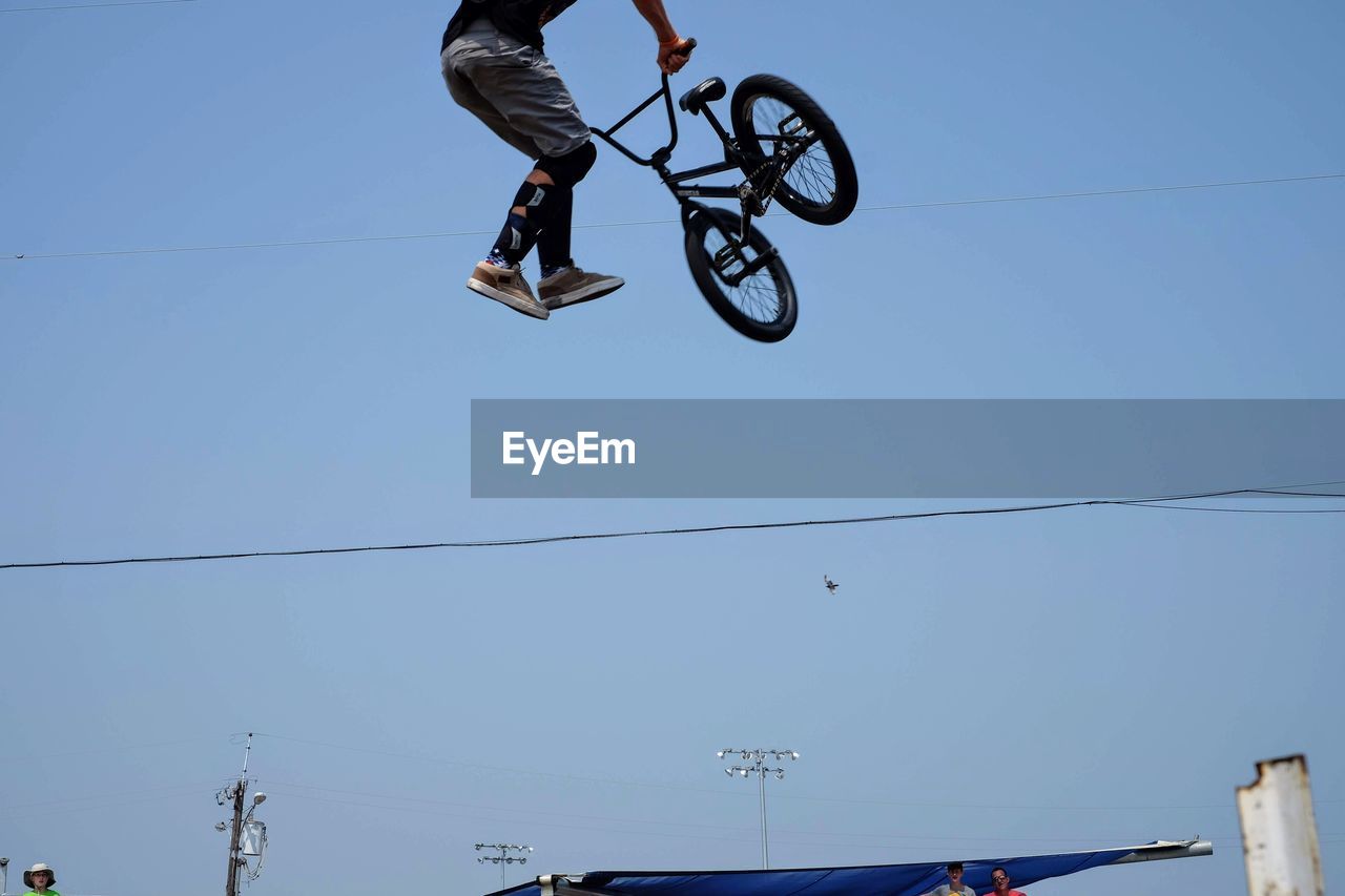 Low angle view of man doing stunt with bicycle against clear blue sky