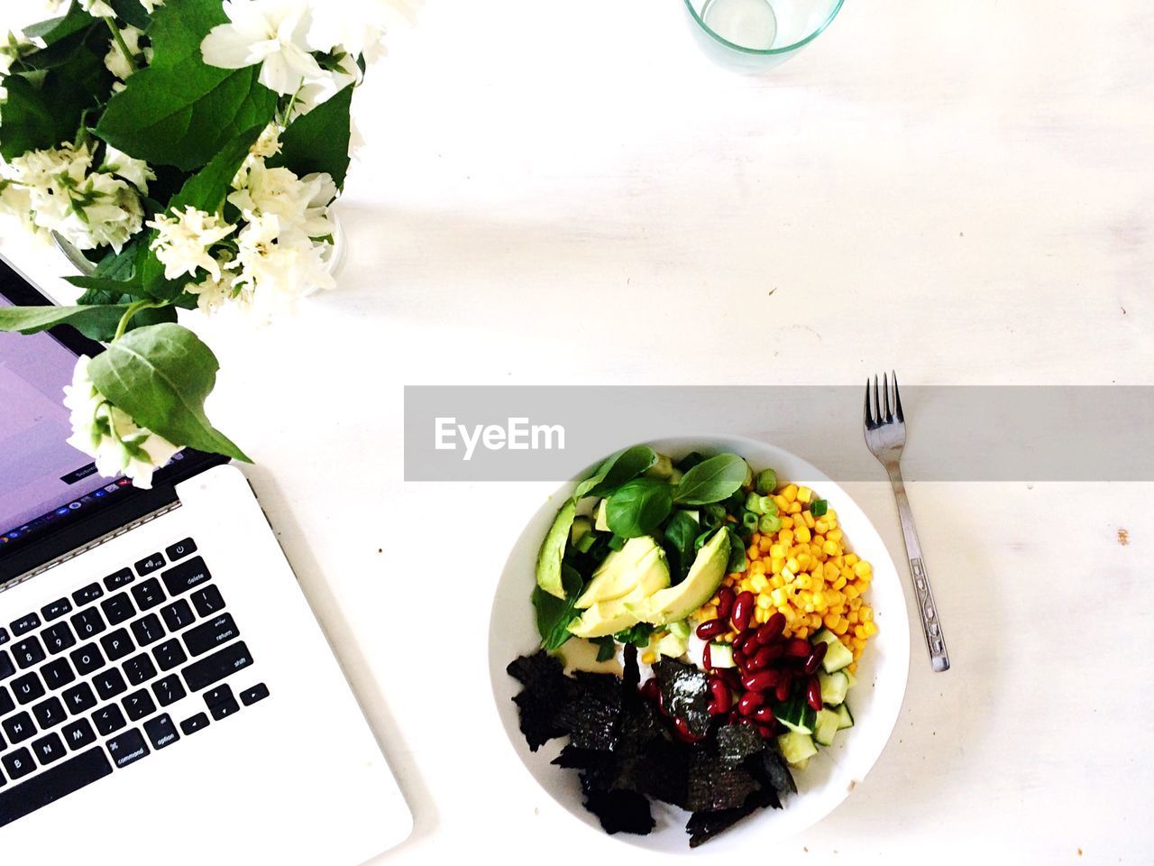 Bowl of salad by laptop on table