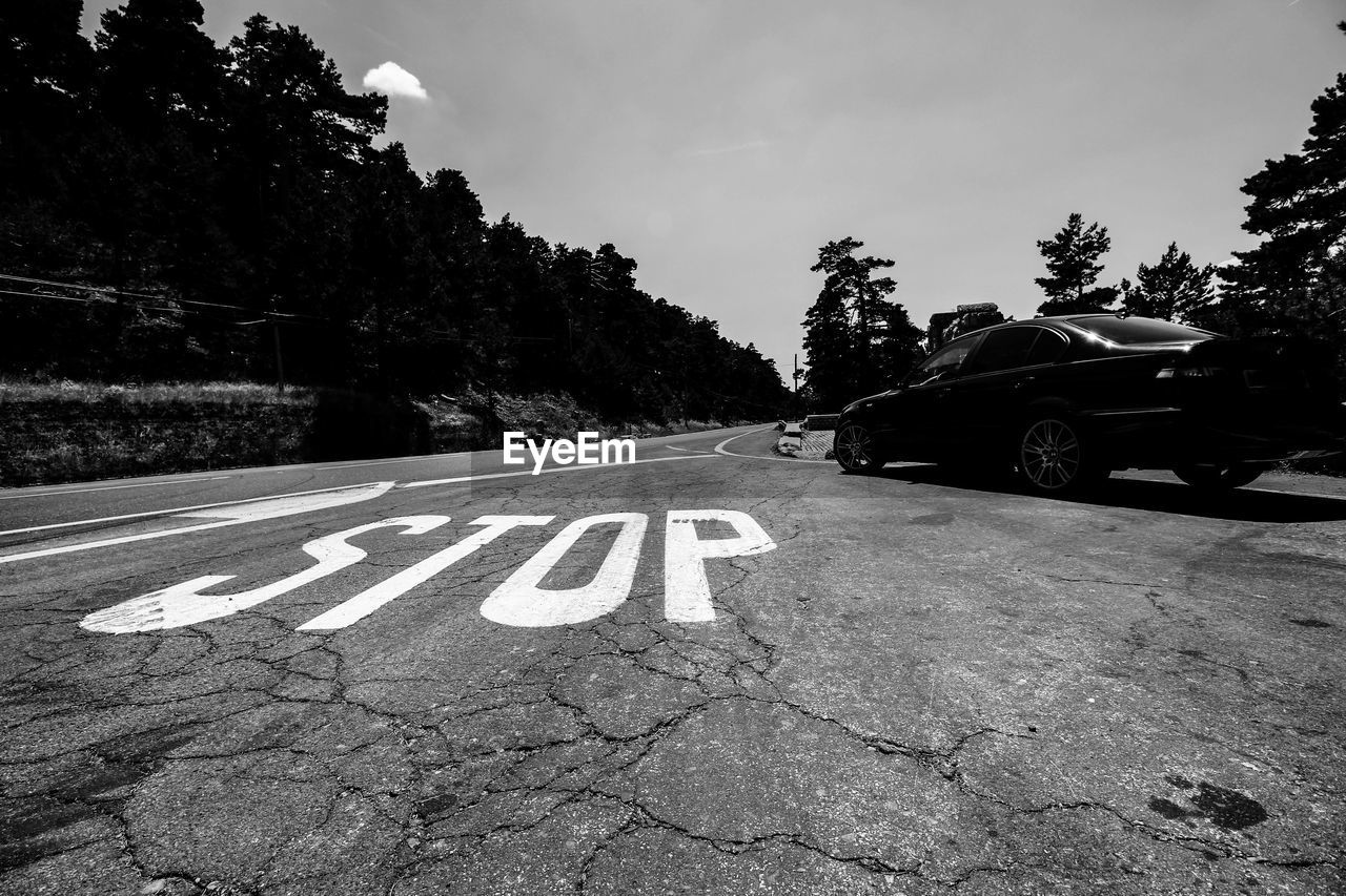 Stop sign by car on road during sunny day