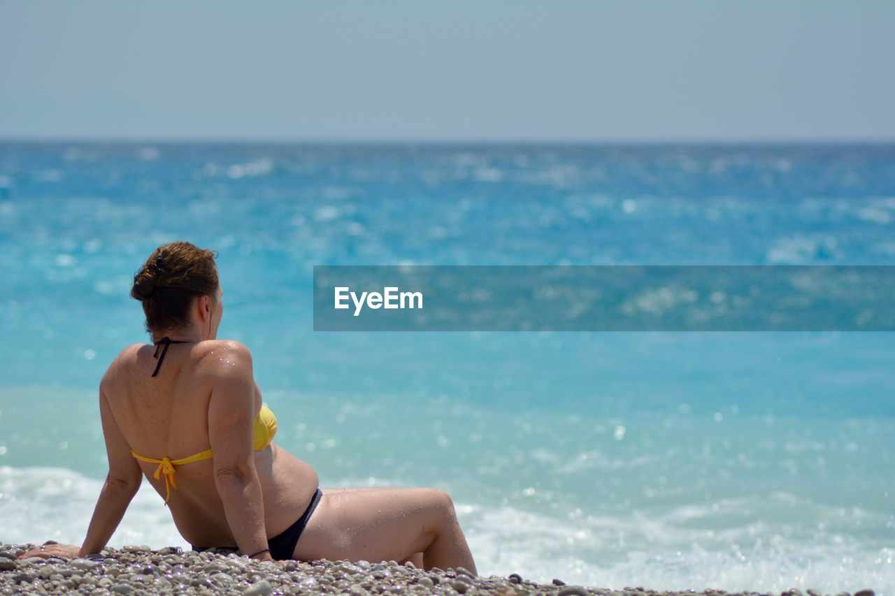 Woman in bikini sitting on shore at beach