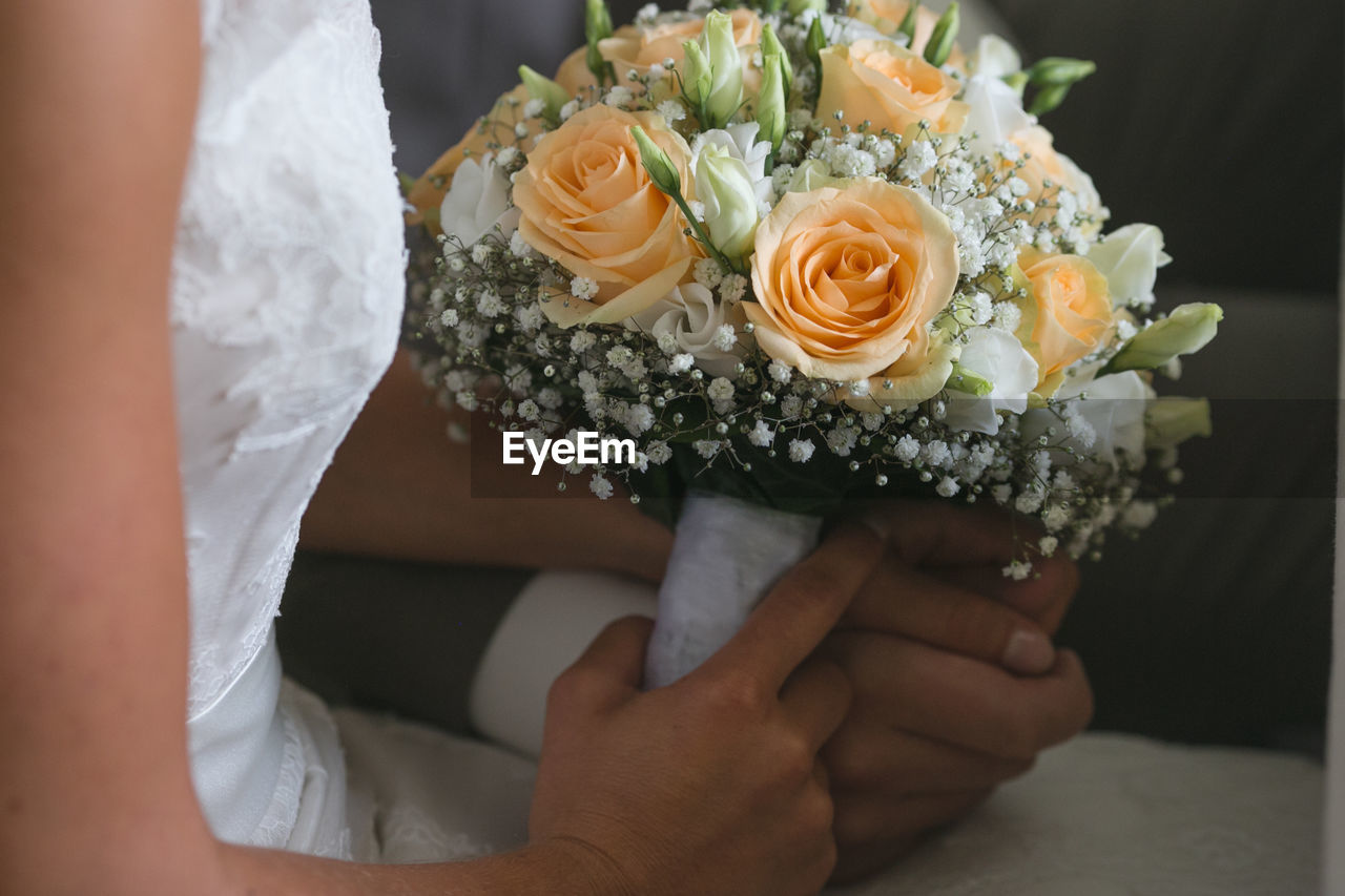 Midsection of bride and groom holding rose bouquet