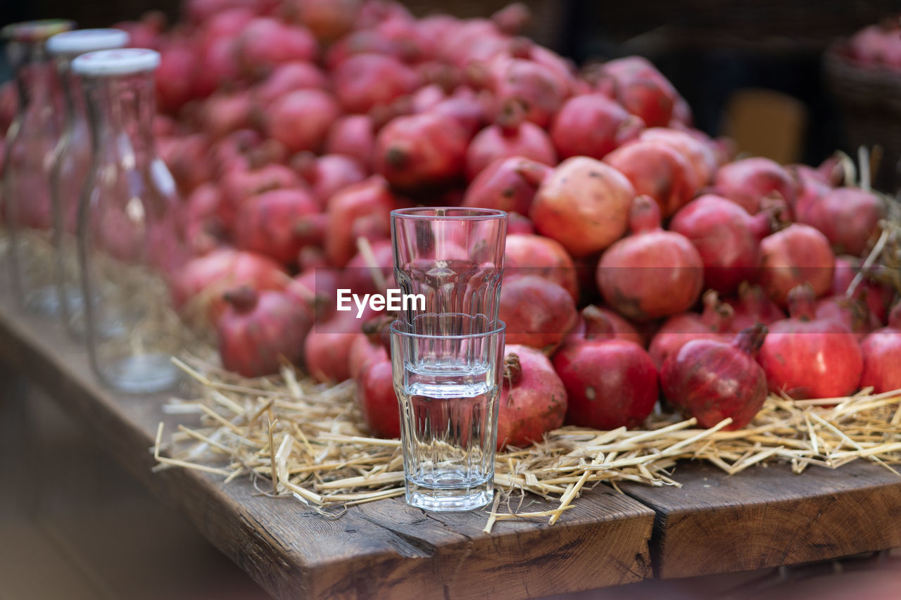 Harvest of ripe pomegranates for juice with glass and bottles on wooden table at farmers market