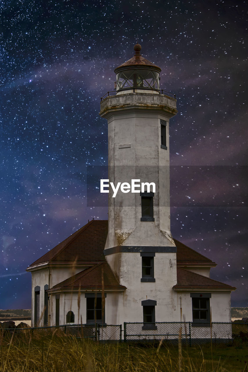 Low angle view of lighthouse by building against sky at night