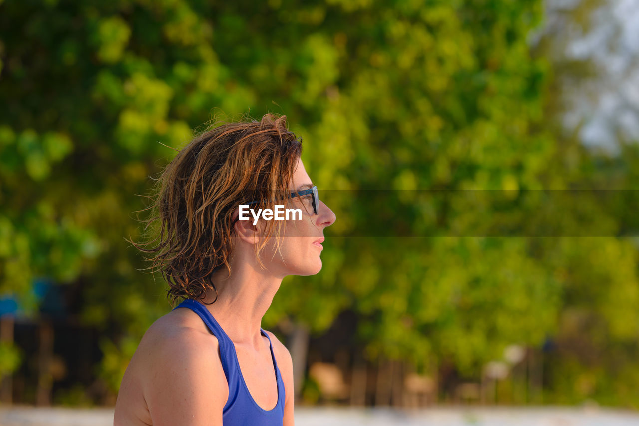 Portrait of young woman looking away against trees