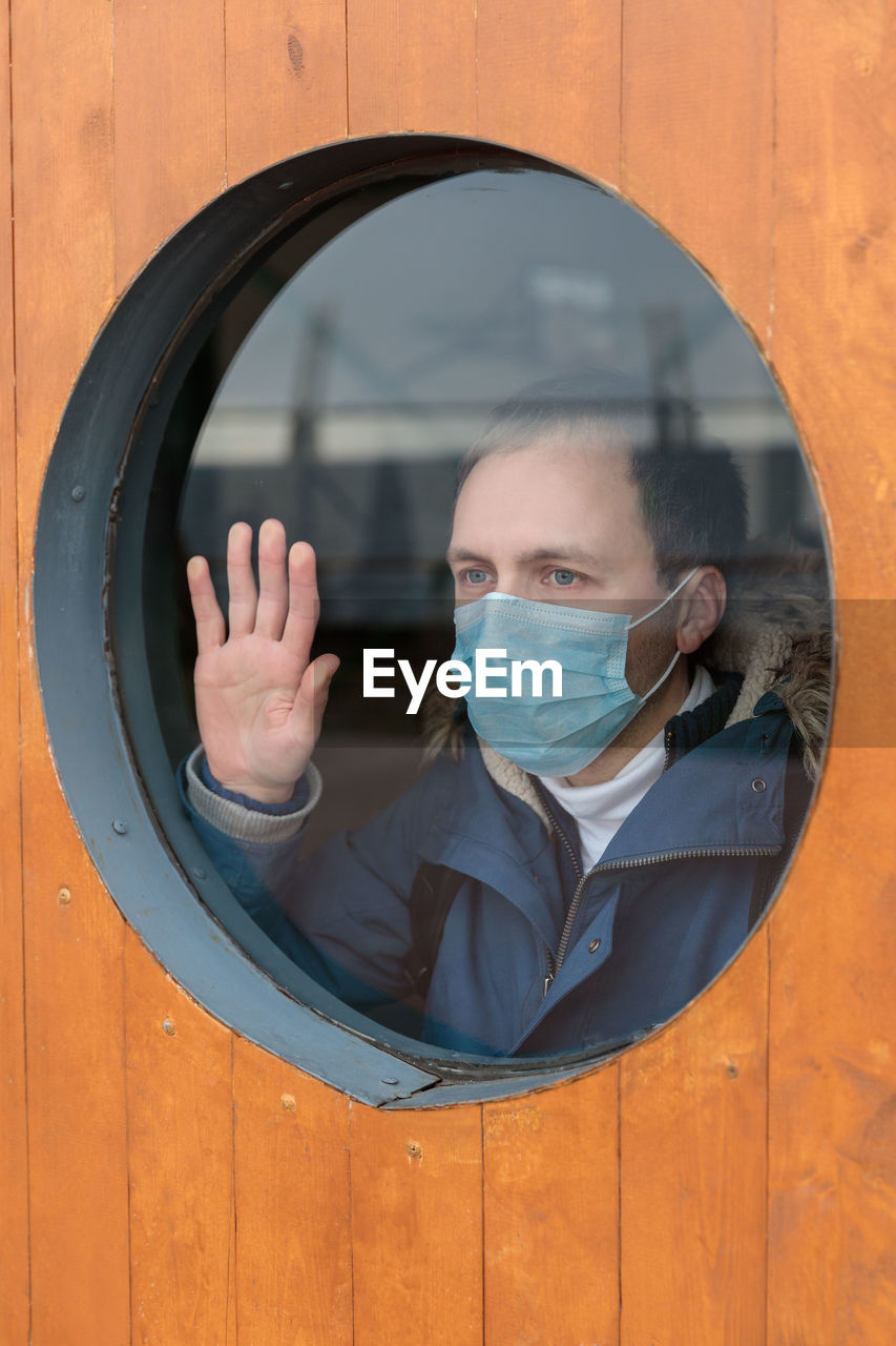 Man wearing mask while looking through window