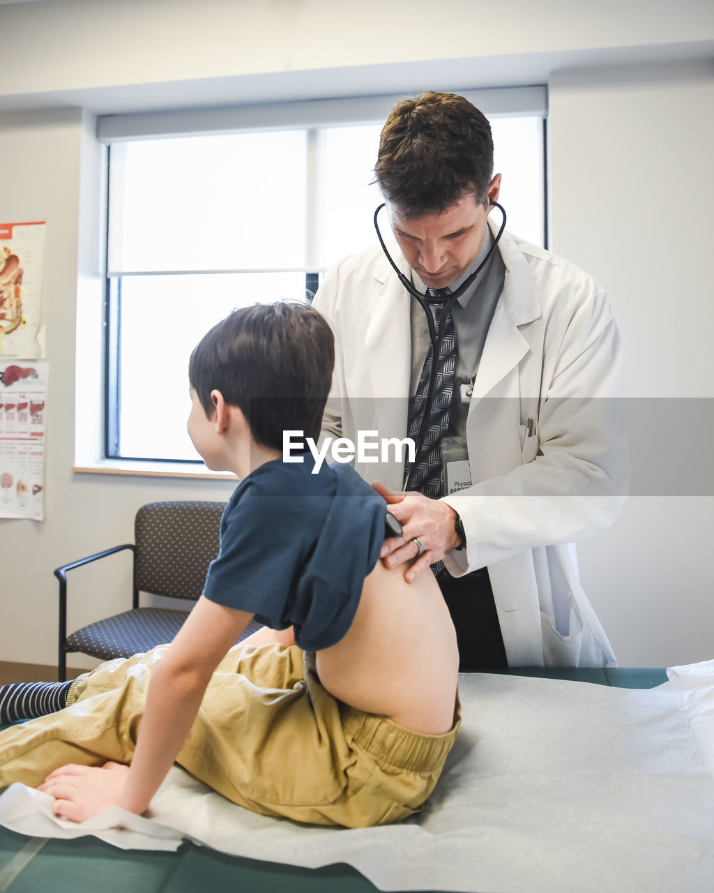 Doctor with stethoscope on a child's back on a clinic exam table.