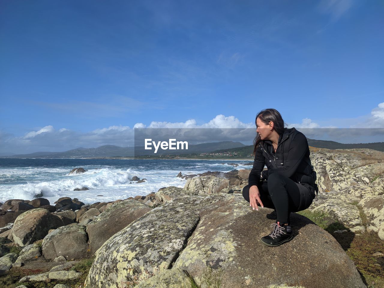 Full length of man sitting on rock at beach against sky