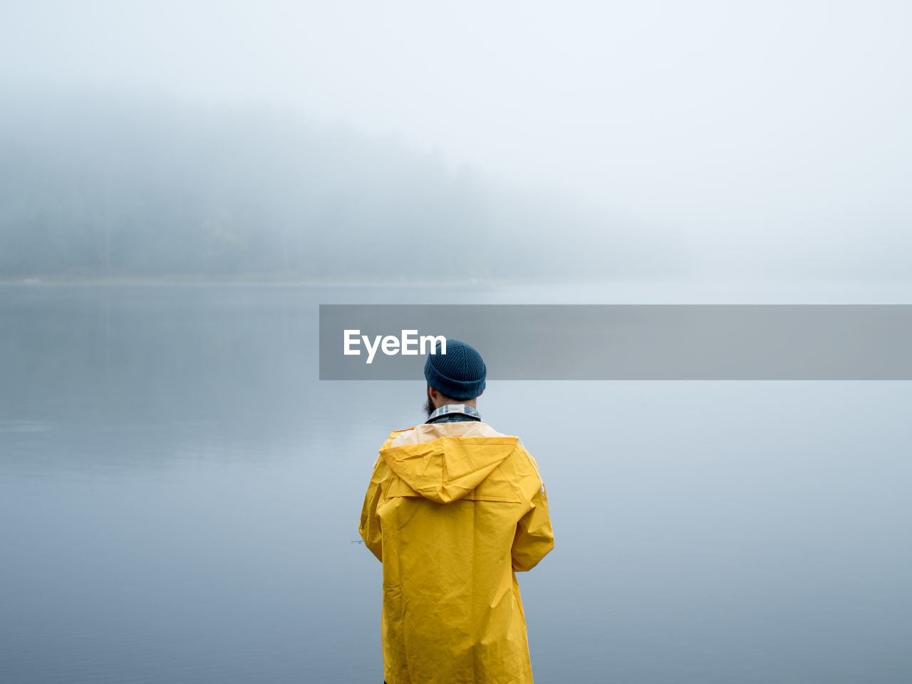 Rear view of man standing by foggy lake