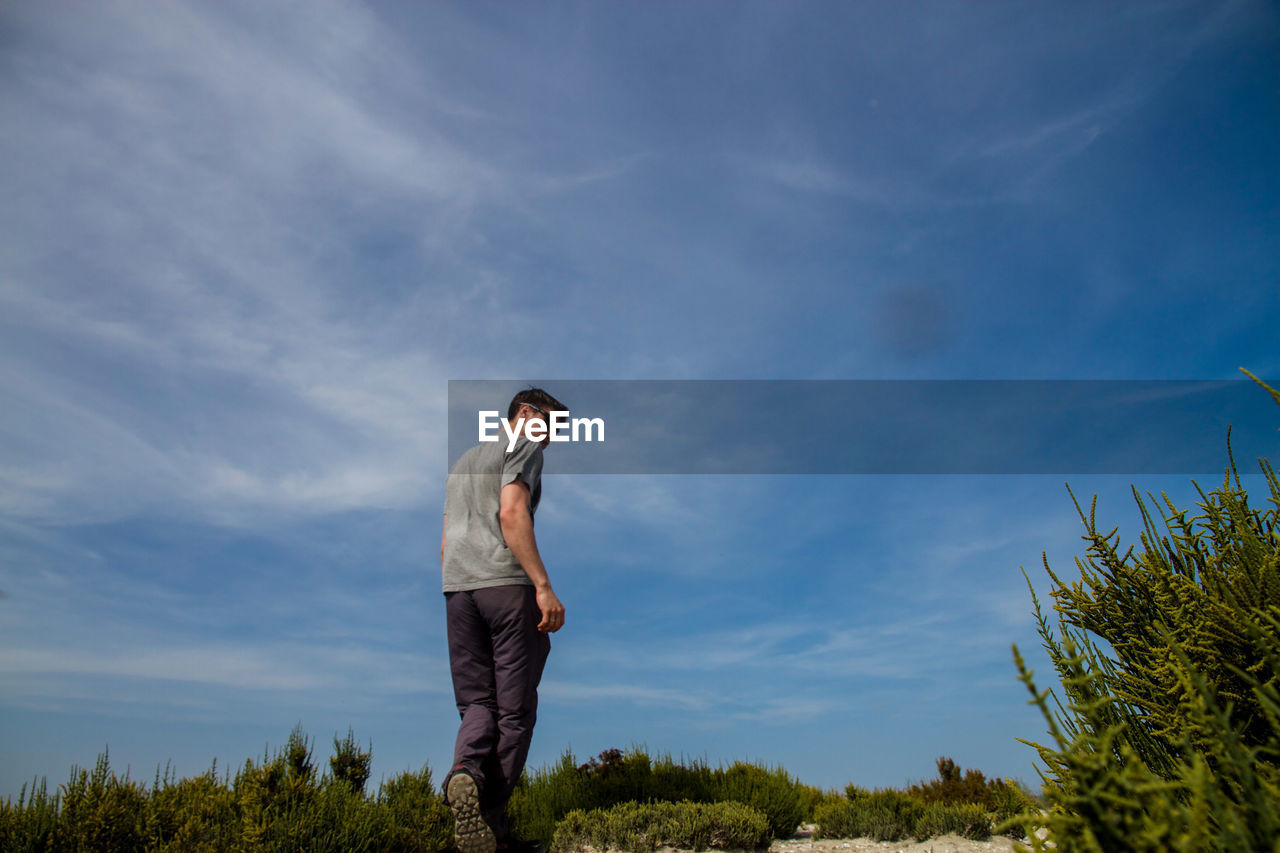 Rear view of man walking on field against blue sky