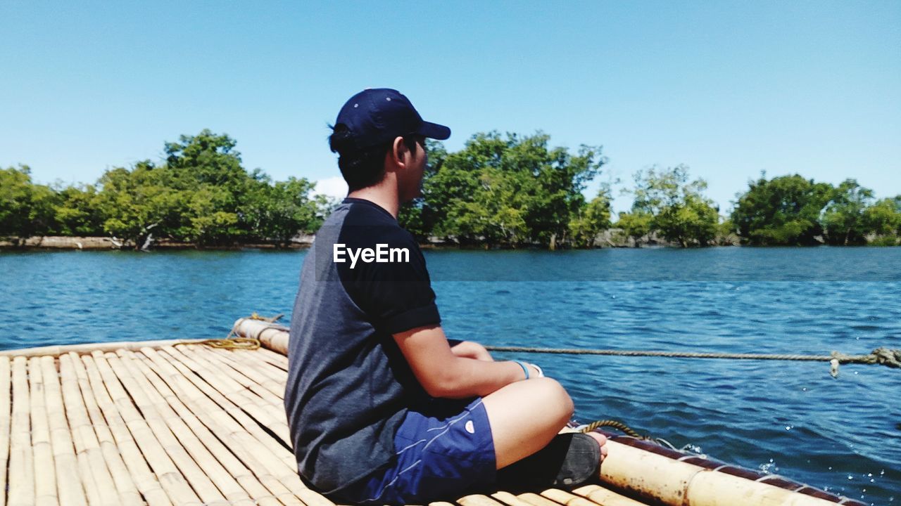 FULL LENGTH OF MAN SITTING ON BOAT AGAINST LAKE