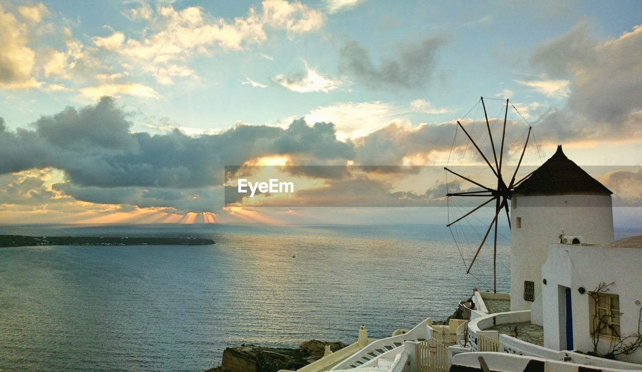 Nature theories- scenic view of sea and traditional windmill against sky during sunset